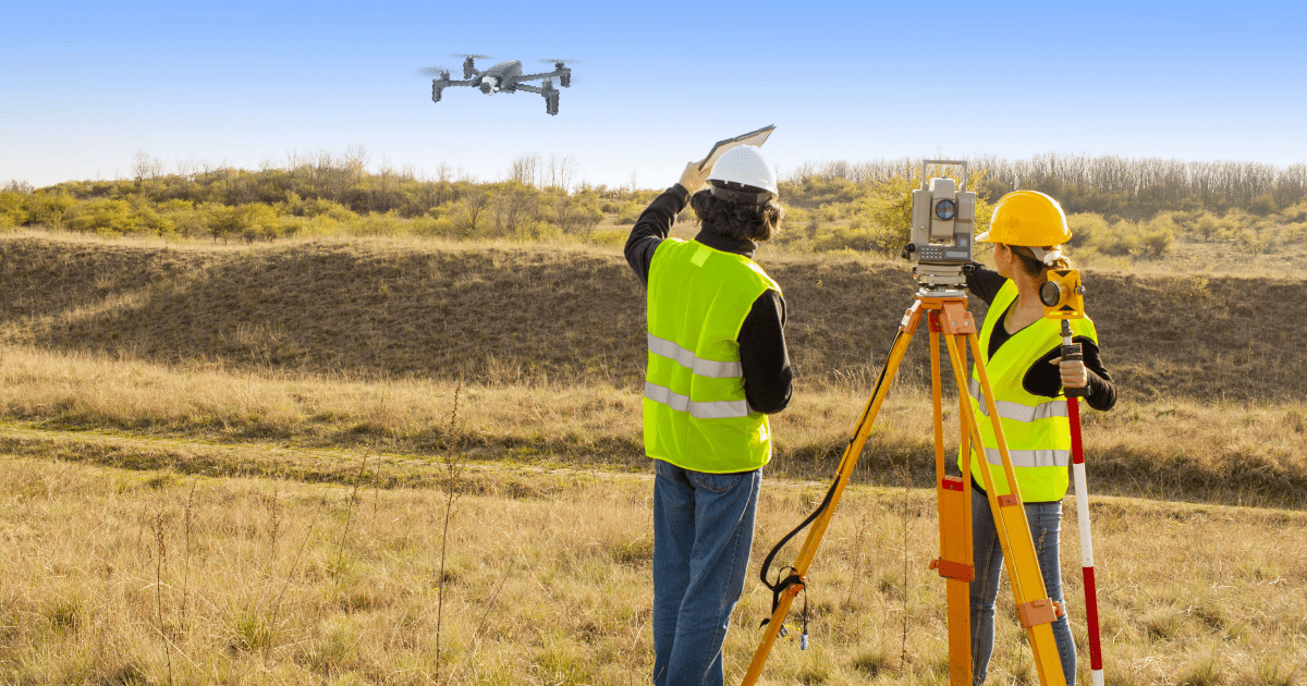 Equipo de topografía trabajando con estación total mientras un dron sobrevuela la parcela
